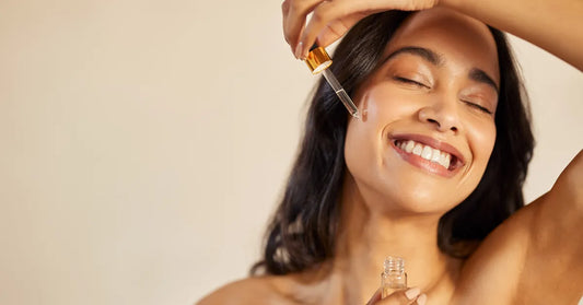 Femme souriante appliquant un sérum à la vitamine E sur le visage pour une peau éclatante et hydratée