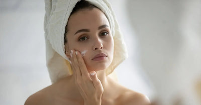 Femme en peignoir appliquant une crème hydratante sur son visage après sa routine de soin pour peau sensible.