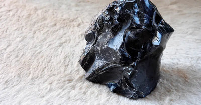 Photo d'un bloc d'obsidienne noire brute posé sur un tissu beige, mettant en valeur sa texture vitreuse et ses reflets naturels