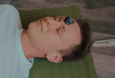 Homme allongé avec une pierre d'obsidienne noire posée sur le front, utilisée pour la méditation et l'équilibre énergétique.