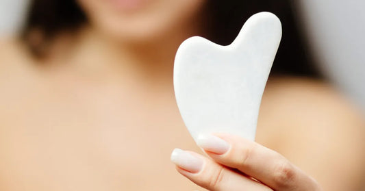 Femme tenant un gua sha blanc pour massage du visage, soin naturel anti-ride et rituel de beauté ancestral
