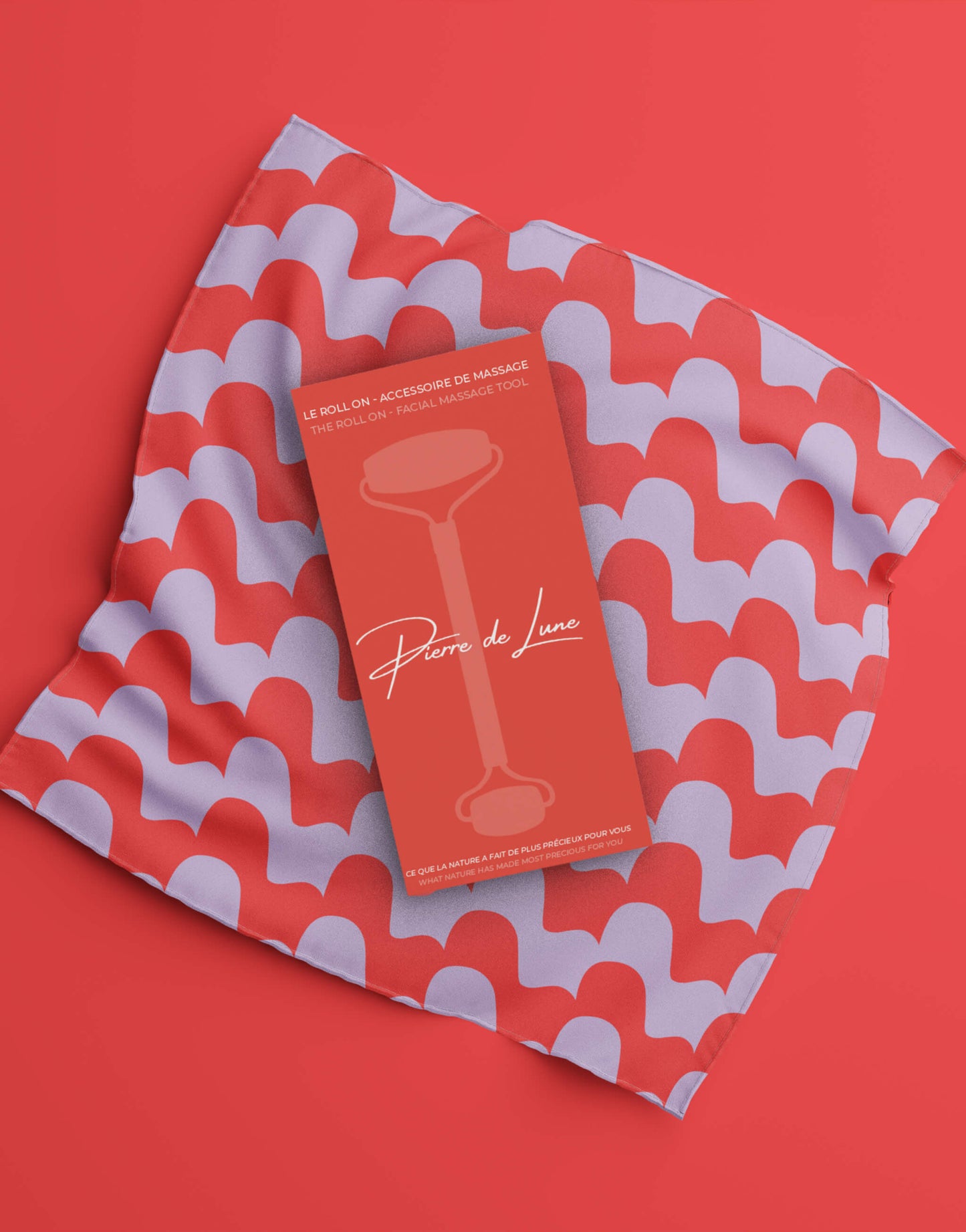 Image montrant le packaging d'un roller en pierre de lune sur un tissu à motifs rouges et violets, avec un design graphique élégant et moderne
