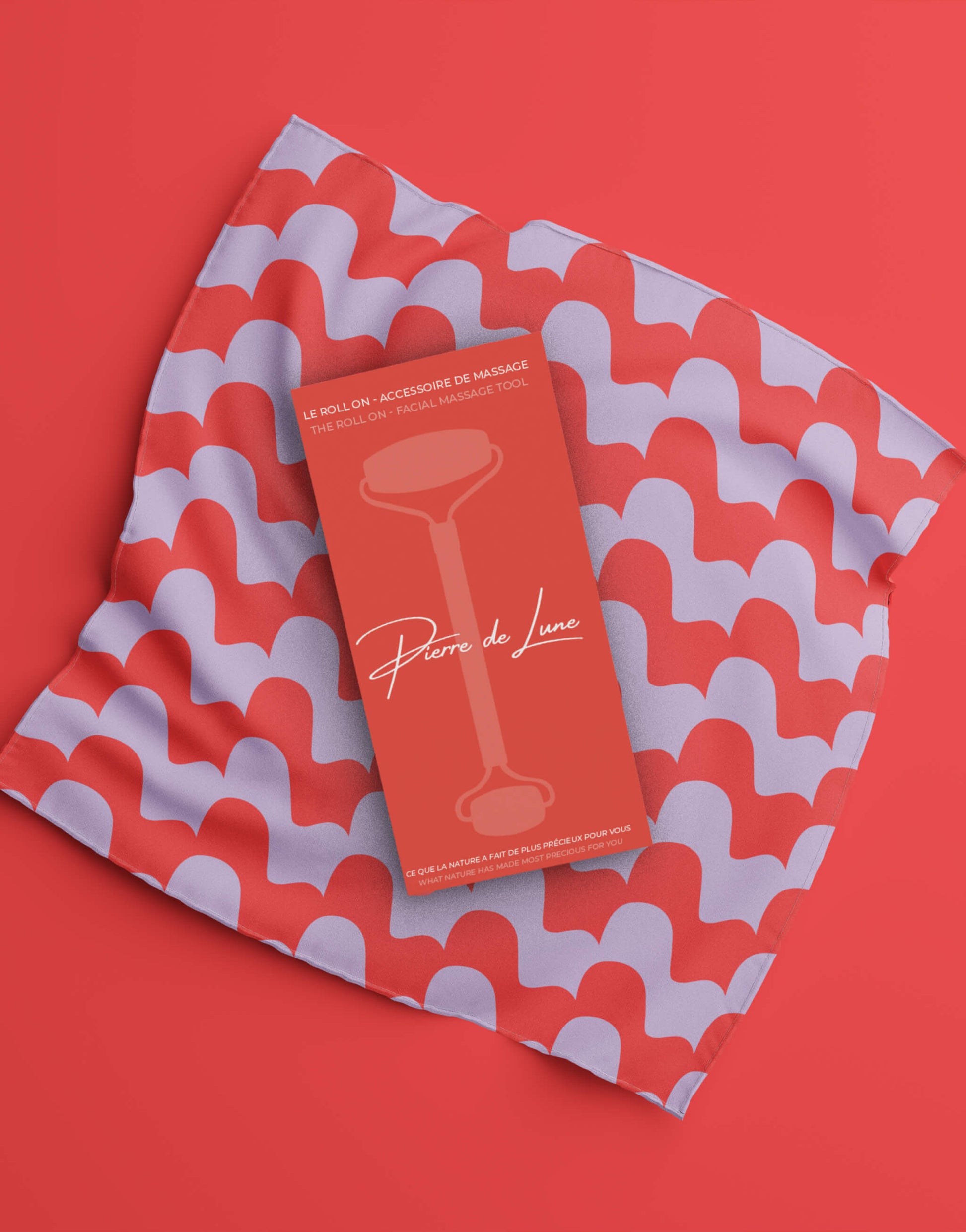 Image montrant le packaging d'un roller en pierre de lune sur un tissu à motifs rouges et violets, avec un design graphique élégant et moderne